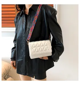 Detail of white quilted crossbody bag with colorful geometric strap and gold hardware