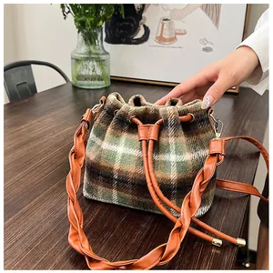 Detail of plaid wool bucket bag with drawstring closure and woven leather shoulder strap