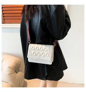 Close-up of a white quilted crossbody bag featuring a colorful woven jacquard strap