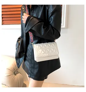 Close-up of a white quilted crossbody bag with a colorful ethnic woven wide shoulder strap
