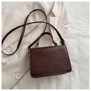 Detail of dark brown leather handbag with gold metal clasp on beige blazer