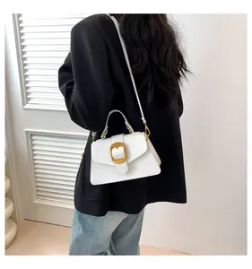 Close-up of a white leather crossbody bag featuring a textured gold metal buckle and strap