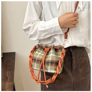 Detail view of plaid bucket bag with drawstring closure and brown leather shoulder strap