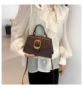 Detail of elegant dark brown leather handbag featuring a textured gold square buckle