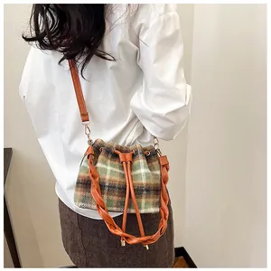 Detail of wool bucket bag with plaid pattern and leather handle worn by a model