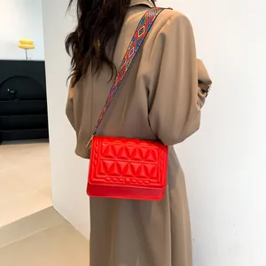 Chic red quilted crossbody bag with patterned wide shoulder strap and geometric texture