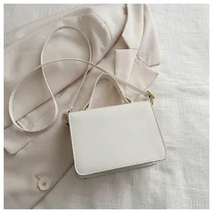 Detail of white leather crossbody bag with gold hardware on a beige blazer background