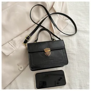 Detail of black leather crossbody bag with gold shield lock and phone for size comparison