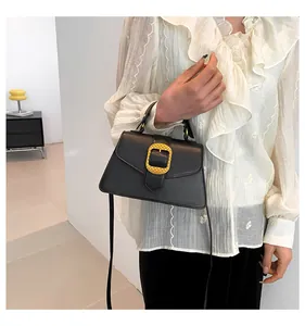 Detail of black trapezoid crossbody bag featuring a golden woven metal buckle and top handle