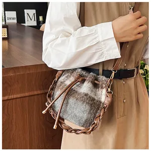 Detail of wool bucket bag with plaid pattern, leather woven handle and gold hardware
