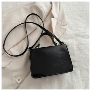 Detail of a black leather crossbody bag on a beige blazer with gold hardware