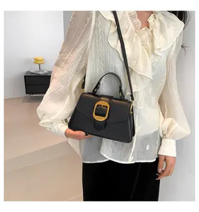Detail of elegant black trapezoid handbag with textured gold metal buckle and leather strap