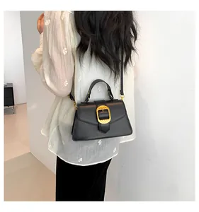 Detail of a black leather crossbody bag with a textured gold square buckle on a model
