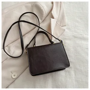 Detail view of dark brown leather handbag with gold metal clasp on a beige blazer