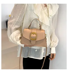 Close-up of beige crossbody bag with gold woven buckle on white shirt background