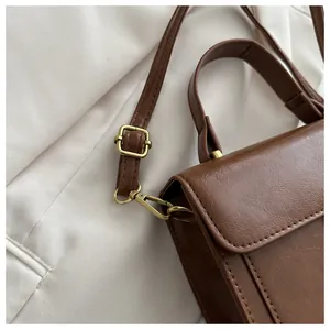 Close-up of golden hardware and leather stitching on a brown crossbody bag
