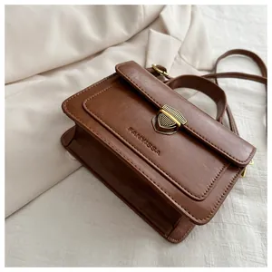 Close-up of retro dark brown square bag showing gold shield lock and leather texture