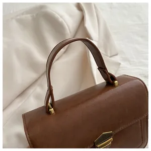 Close-up of retro brown leather handbag featuring bronze metal lock and textured surface