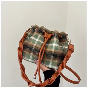 Close-up of wool plaid bucket bag with braided leather strap and golden hardware