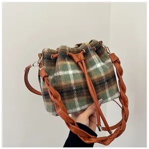 Detail of green and brown plaid wool bucket bag featuring leather braided handle and drawstring