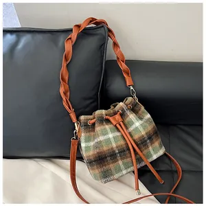 Top view of a plaid wool bucket bag with orange woven handles on a leather background