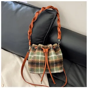 Detail of wool bucket bag showing brown plaid texture and woven shoulder strap