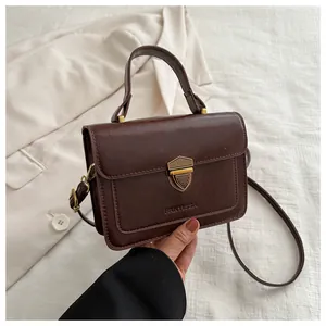 Detail of the vintage dark brown small square bag featuring a gold shield lock and shoulder strap