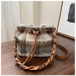Detail of wool bucket bag showing plaid texture, drawstring closure and woven strap