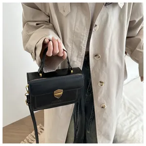 Detail of vintage black leather crossbody bag with golden shield lock and beige trench coat