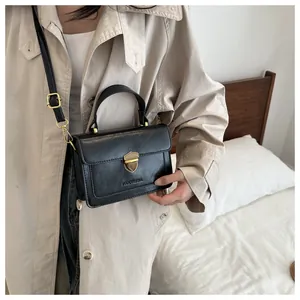 Detail of black leather crossbody bag with golden shield clasp on beige trench coat