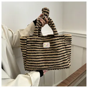 Detail of striped plush tote bag with logo tag held by model in cream coat