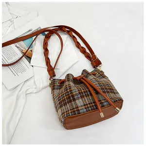 Detail of tweed bucket bag showing plaid texture and woven wide shoulder strap