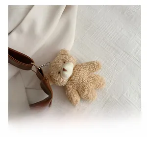 Close-up of a cute khaki plush bear pendant attached to a vintage brown leather bag