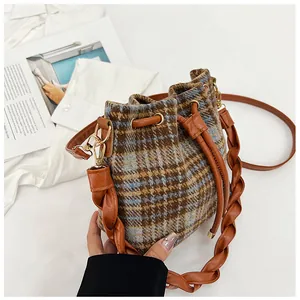 Detail of plaid bucket bag featuring drawstring closure and woven leather handle with gold hooks