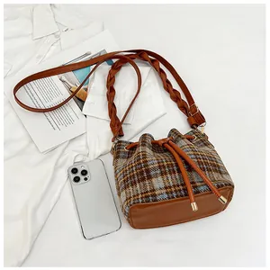 Detailed view of plaid wool bucket bag with woven leather strap and drawstring closure
