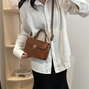 Retro caramel square handbag with top handle and gold latch shown on a shelf