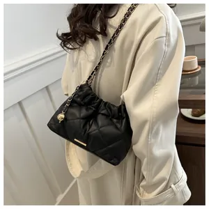 Detail of black quilted bucket bag featuring gold logo plate and chain shoulder strap