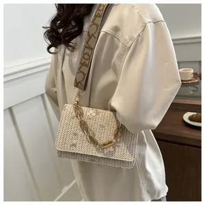 Detail of floral embroidery and resin chain on a cream woven crossbody bag