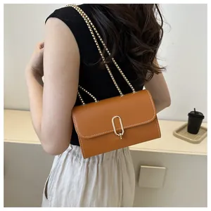 Détail d'un sac carré en cuir caramel avec fermoir ovale doré et coutures blanches