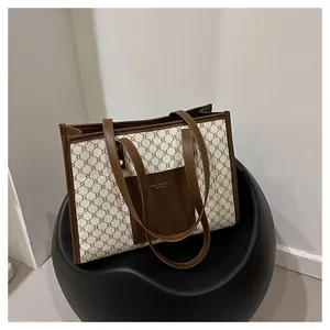 Close-up of a large beige monogram tote bag with brown trim on a modern black stool