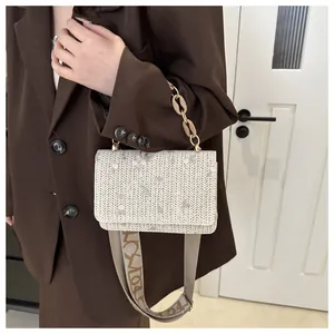 Close-up of woven cream square bag with floral embroidery and textured strap detail