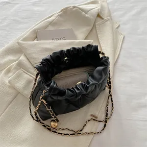 Quilted black bucket bag with gold chain and metal ball detail on white blazer