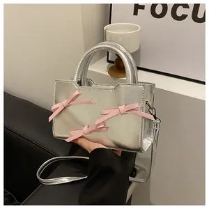Détail du sac à main en cuir verni argenté avec nœuds roses sur fond de canapé noir