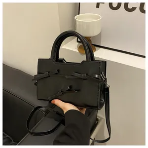 Détail du sac à main en cuir verni noir avec nœuds décoratifs et poignée supérieure robuste