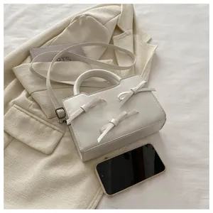 Détails du sac blanc en cuir verni avec nœuds, poignée ronde et finitions métalliques
