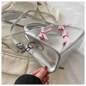 Détail du sac à bandoulière argenté avec trois nœuds roses décoratifs et poignée supérieure
