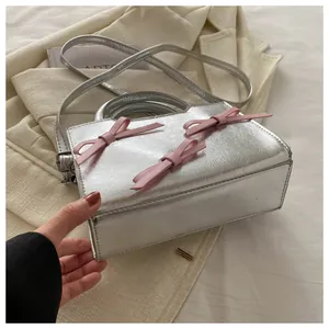 Détail du mini sac argenté texturé avec trois nœuds roses sur un drap blanc