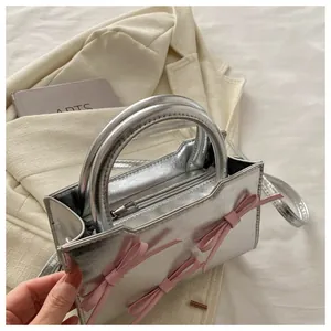 Détail du sac carré argenté métallisé avec trois nœuds roses et poignées rondes fixes