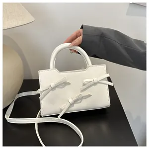 Détail du mini sac blanc avec trois nœuds 3D et une poignée supérieure incurvée
