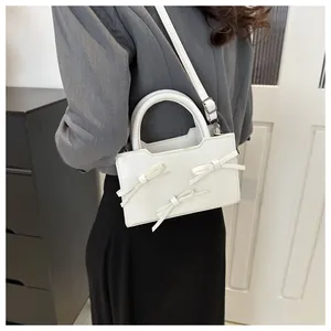 Détail d'un petit sac blanc en cuir verni avec nœuds et bandoulière réglable sur le corps